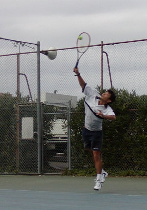 Serve Motion. Contact at full length with arm extended, racket coming up from behind. The ball being struck in mid-air is caused by the throwing jack-knife spring motion of the body.